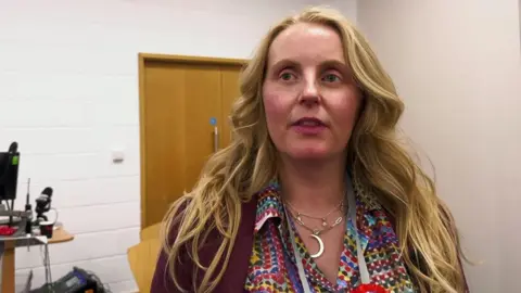 Naomi Tweddle at the election count she has long blond hair and is wearing a patterned shirt and purple jacket