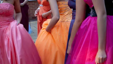 Getty Images Girls at a school prom wearing pink, purple and orange prom dresses. 