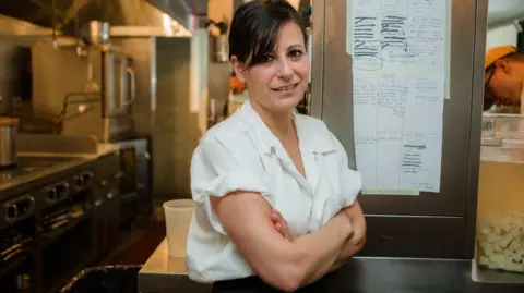 Amanda Cohen Amanda Cohen stands in her restaurant kitchen with her arms crossed