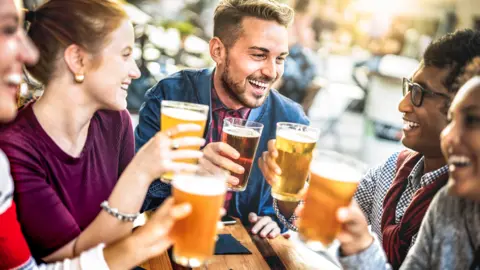 A group of happy men and women enjoying pints of beer whilst seated at a table outside a pub
