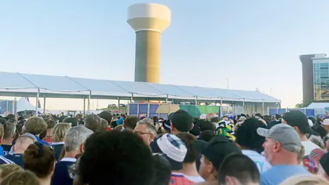 Age crowd of football fans, viewed from behind, massed outside a stadium at a security checkpoint.