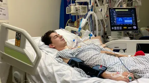 The Air Ambulance Service A man lies in a hospital bed, attached to monitors and tubes, with a screen showing information about his condition