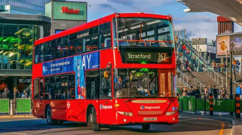 A London bus pulling into a stop at Stratford. The Westfield shopping centre is visible in the background. 