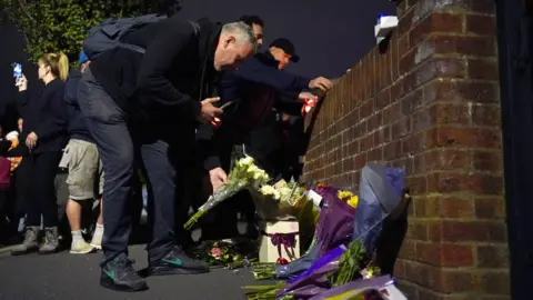 Представники ЗМІ залишають квіти біля Мідхерст Гарденс в Аксбріджі.