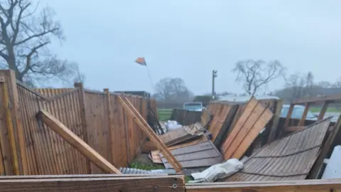 The Owl Experience Rescue Sanctuary Brown fence panels on their side and on the floor after high winds, with trees in the background. 