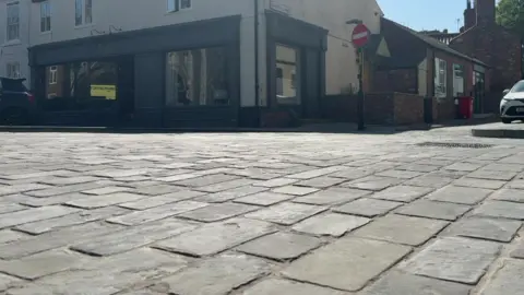 A close up of the newly laid stone pavers from ground level. A shop with grey frontage can be seen in the background.