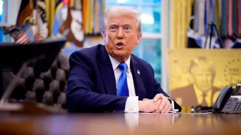 Getty Images President Donald Trump speaks before introducing a $100,000 fee for H-1B visas. He is pictured in a suit and a blue tie. 