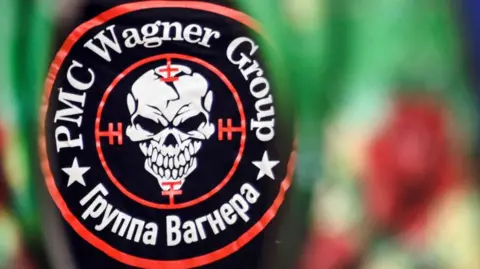 A logo for the Wagner group, bearing a grinning skull and the words "PMC Wagner Group"