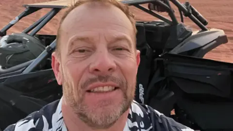 Simon Rourke Simon Rourke in the desert with a dune buggy in the background