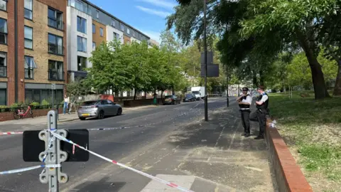 Rory Bibb/BBC Two police officers standing on the pavement behind police tape. 