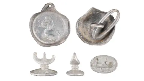 A silver cufflink with an image of a woman and and a seal matrix with a two people in a boat.