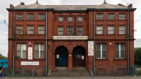 Peter McDermott/Geograph Crossley House, a three-storey red brick building, with two arched doorways and blue railings outside