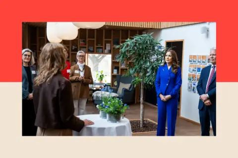 Getty Images Queen Mary pictured in a bright blue suit with other people ina room with a tree and soft furnishings