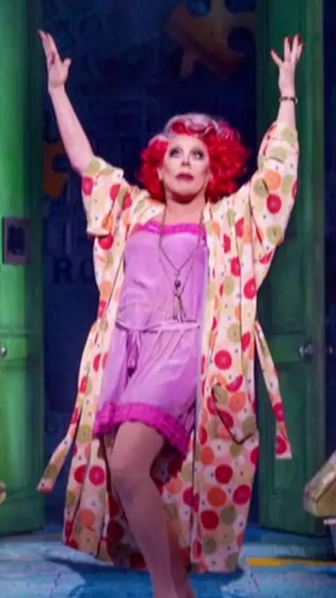 drag queen la voix on stage in colouful dressing gown and pink pyjamas.