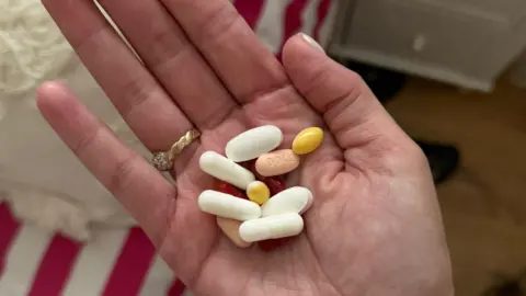Regan Sparks A woman holds a number of tablets and pills, in her palm - medication which she takes for cystic fibrosis. The tablets are white, yellow and pink.