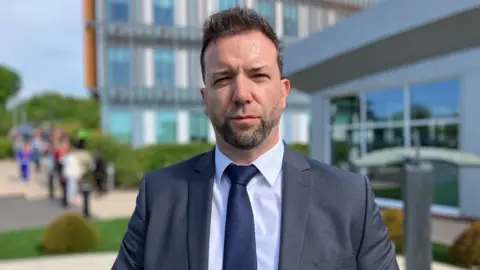 Detective Superintendent Andrew Williams from Counter Terrorism Policing Wales is wearing a grey suit with a navy tie and looking straight at the camera.