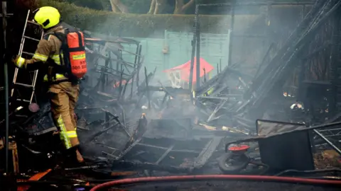 South Yorkshire Fire & Rescue A firefighter stood in a badly fire-damaged garden. The photo shows the ruins of what could be a shed, as well as a charred wheelbarrow and a fire-damaged children's play house.