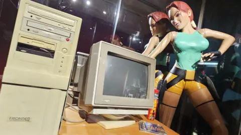 Supplied A retro desktop computer on a desk next to a Larazaade bottle and a life-sized statue of Lara Croft