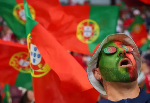 Reuters A Portuguese fan wearing full face paint and sunglasses looks up to the sky in front of a sea of Portuguese flags