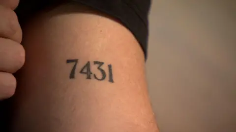 John Nellis A tattoo that shows the number seven four three one, it is on an arm