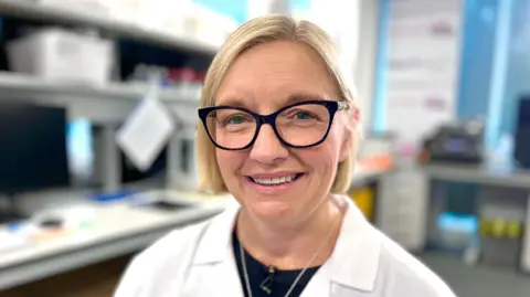 Louise Jopling with blonde hair and large glasses wearing a lab coat