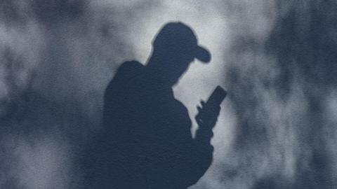 A shadow of a man in a baseball cap holding a phone.