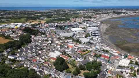 A drone photo taken above Guernsey. There is a number of properties and there is a beach to the right where the tide is out.