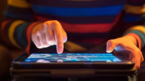 Getty Images Man in striped jumper holding iPad