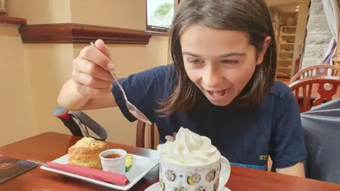 Kerry-Anne Finn eating in a cafe, he is excited by a hot chocolate with whipped cream and about to dig in with his spoon