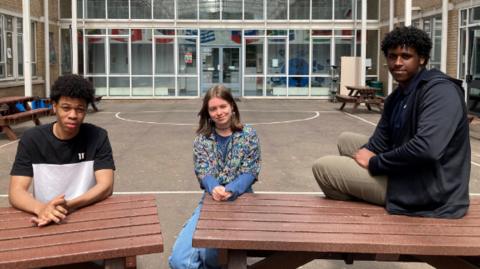 Zach, Jess, Abdirisaq sat on benches outside their college