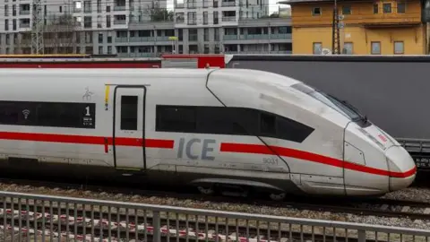 Front end of a German ICE train, travelling from left to right. Buildings can be seen in the background.