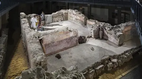 Historic England Roman ruins which have models of Romans inside talking. The ruins are encased by a protective building