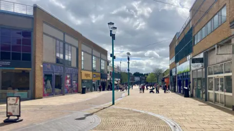 General view of Huyton with shops on both sides of a wide pedestrianised road.