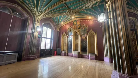 Interior shot of an ornately decorated room, with a gold and green ceiling and golden niches in a wall