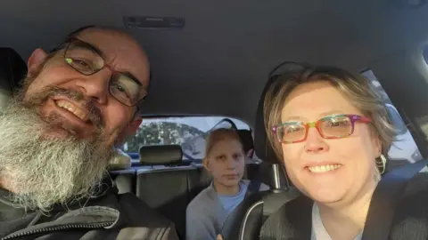 Family photo  Bethany in the back seat of a car with her father Martin and mother Tina 