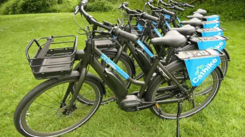A picture of a number of blue bikes pictured on a piece of grass. They are black with blue detail.