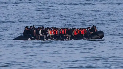 An overloaded inflatable boat sails through waves on a grey day. 