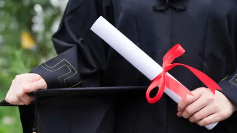 An anonymous stock shot of a hand in graduation robes holding a university degree