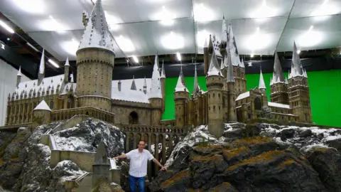 Gary Tomkins The Hogwarts castle model at Leavesden Studios in Watford, shown indoors with snow‑covered towers and spires, with film art director Gary Tomkins standing in the foreground for scale. There is a green screen in the back. Gary is wearing a white shirt and blue jeans.