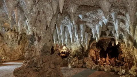 Chris Howard A wide interior view of a grotto lined with dense crystal formations hanging from the ceiling and covering the walls.
