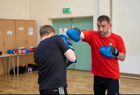 Man in red t shirt wearing fighting pads spars with another man