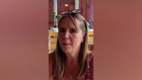 Mia Hansson looking straight at the camera. She wears a pink floral patterned top. She has glasses propped on her forehead.