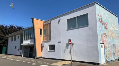 The exterior of the Rollercoaster Youth Centre in Bridgwater. It is a two storey building with large windows on the top floor. One side of the building has a mural on the side.
