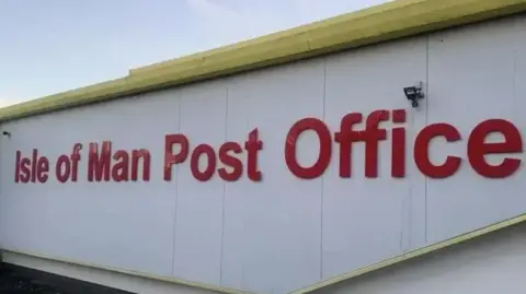 An Isle of Man Post Office sign on the side of the sorting office, which has red lettering on a white wall.
