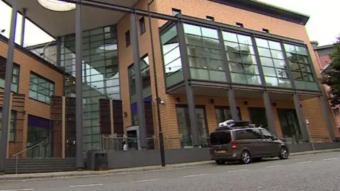 BBC A large brown brick and glass municipal building. A grey van is parked outside.