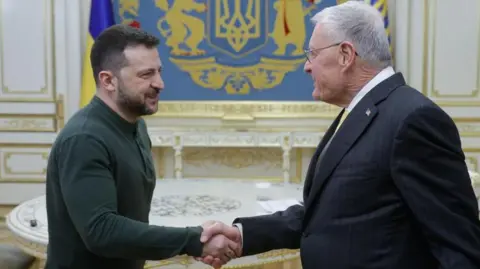 Ukrainian President Volodymyr Zelensky, wearing a green top, welcomes US special presidential envoy for Russia and Ukraine Keith Kellogg with a handshake