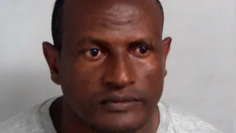 Essex Police A custody mugshot of Hadush Kebatu, who is wearing a grey sweater and has cropped black hair.