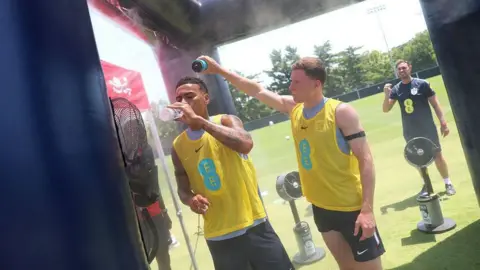 England players trying to cool off in the heat during training - Elliot Anderson is pouring water over Jude Bellingham