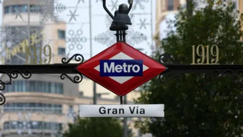 Reuters Connect A Madrid metro sign at the entrance to the Gran Vía station, hanging from a metal railing, with gold letters reading '1919' on either side.