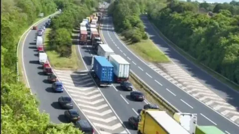 A traffic camera image from above of the A14 dual carriageway. There are long delays of vehicles. There is also a slip road that has been backed up with vehicles. 